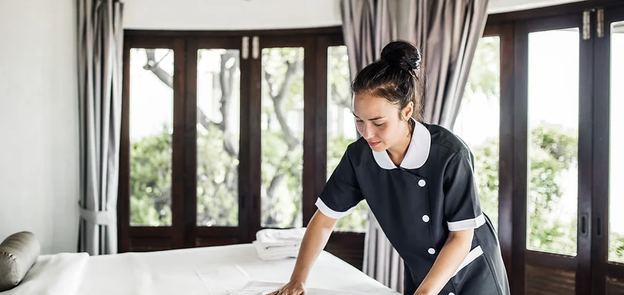 Housekeeper making bed in hotel room.