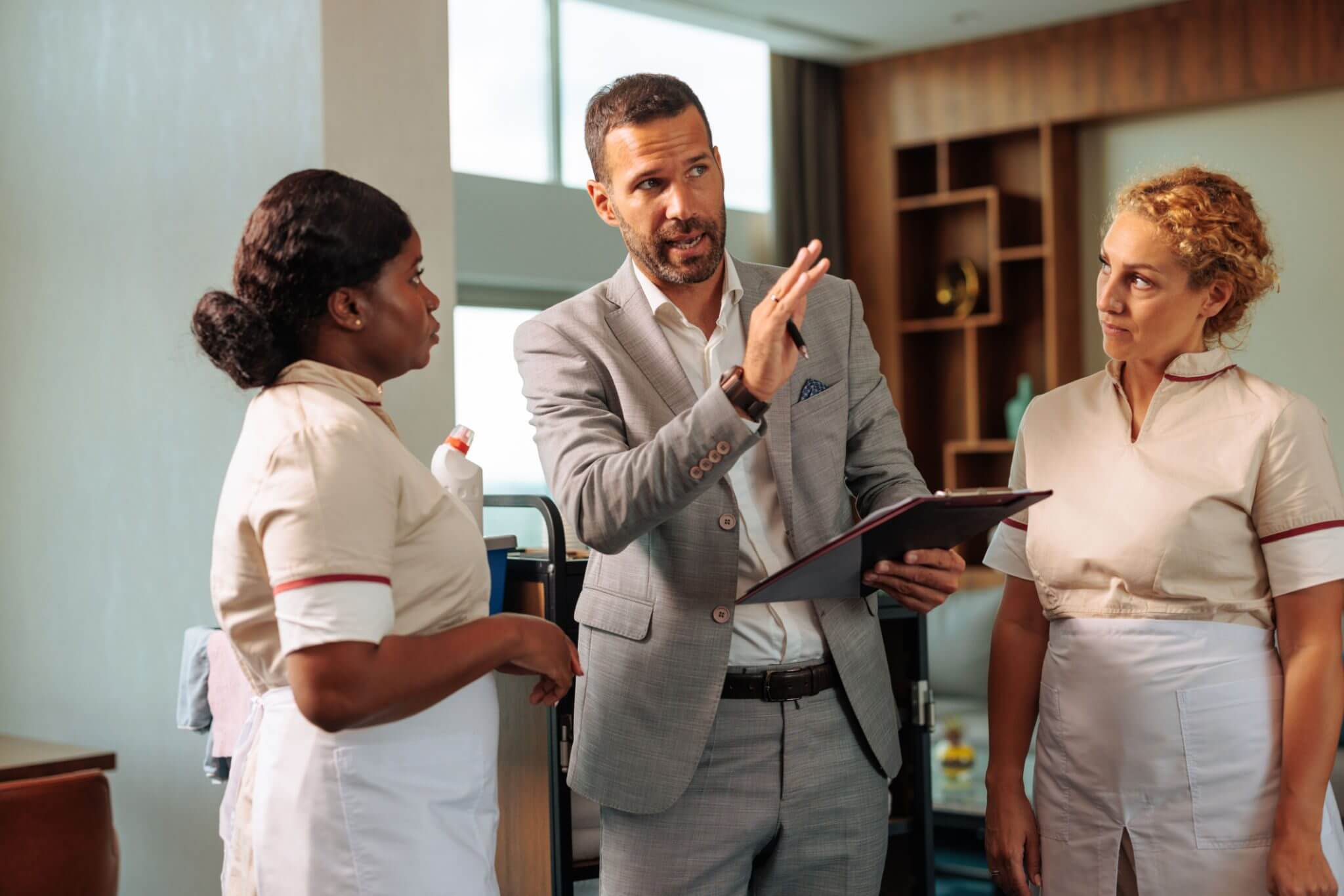 A man in a suit discusses something with two women in nursing uniforms.